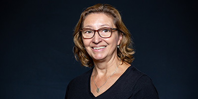 Portrait of a faculty member wearing glasses and a black top, smiling against a dark blue background.